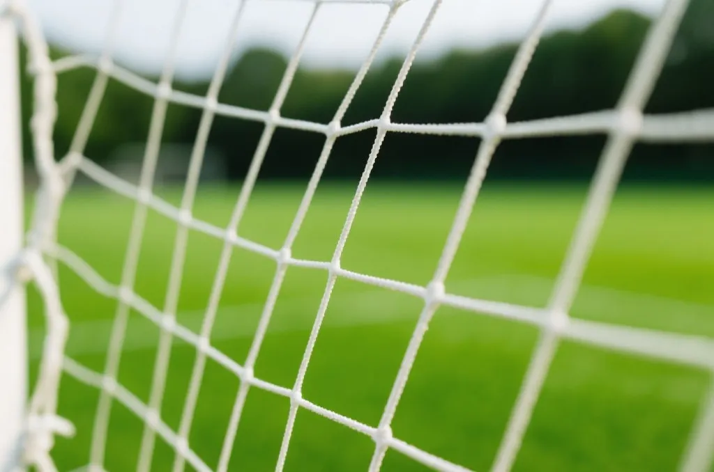 Detailed close-up of a white soccer goal net with a blurred green soccer field in the background
